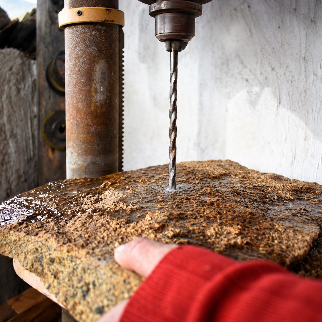 Una mano sostiene una laja de piedra mojada bajo la broca de un taladro de pedestal.